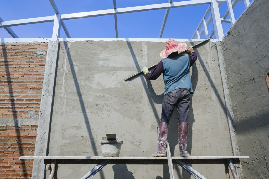 Builder worker on wooden platform is polishing concrete wall in construction site