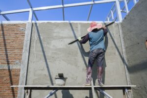 Builder worker on wooden platform is polishing concrete wall in construction site
